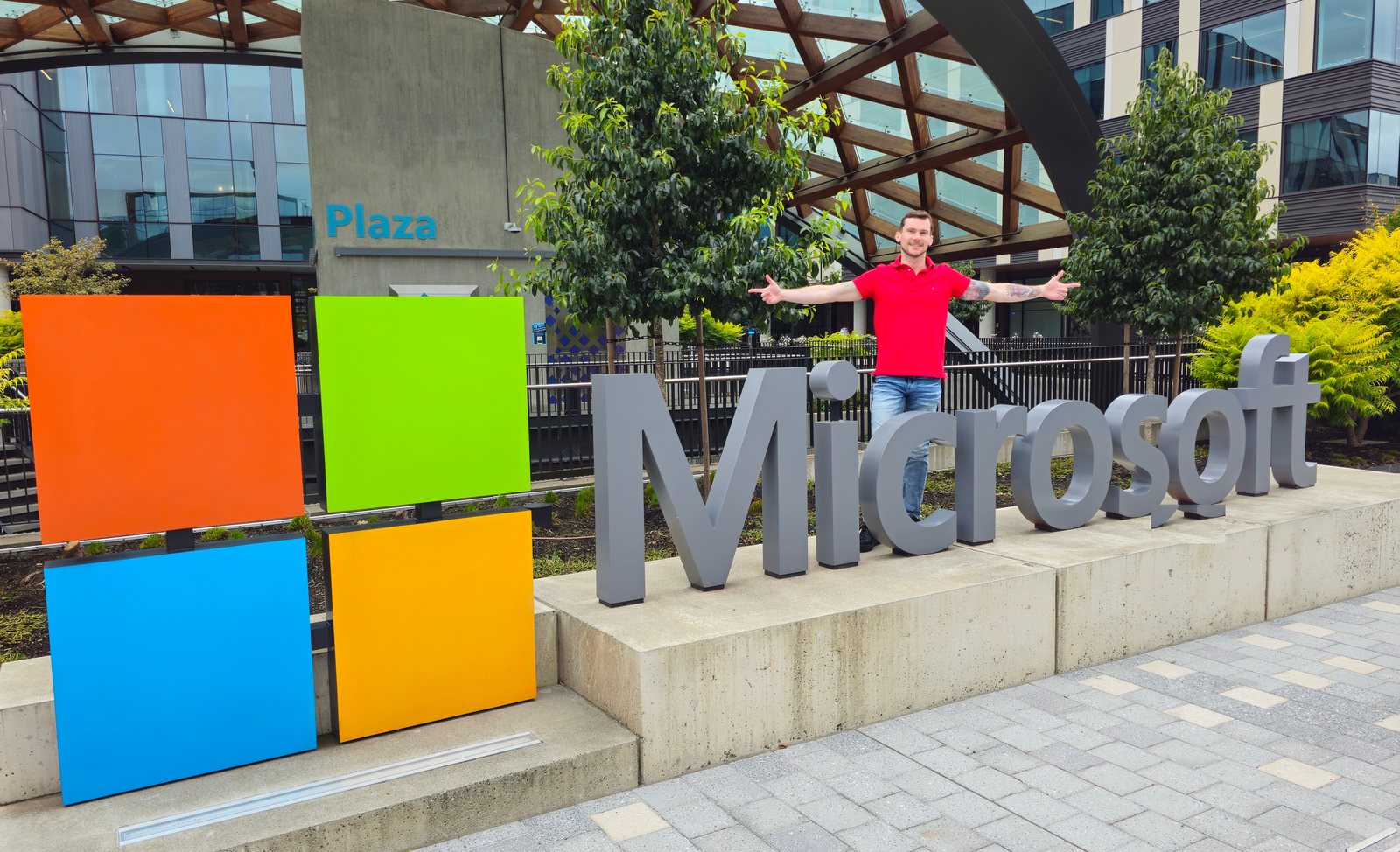 Bryan Totty in a red polo with arms outstretched behind the Microsoft logo sign on the Redmond campus