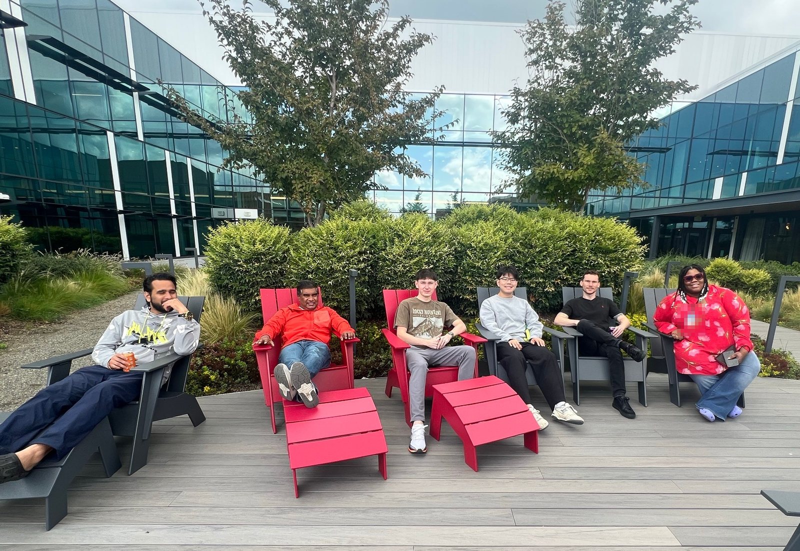 Team members relaxing in red and gray Adirondack chairs in a courtyard between glass buildings on the Microsoft campus